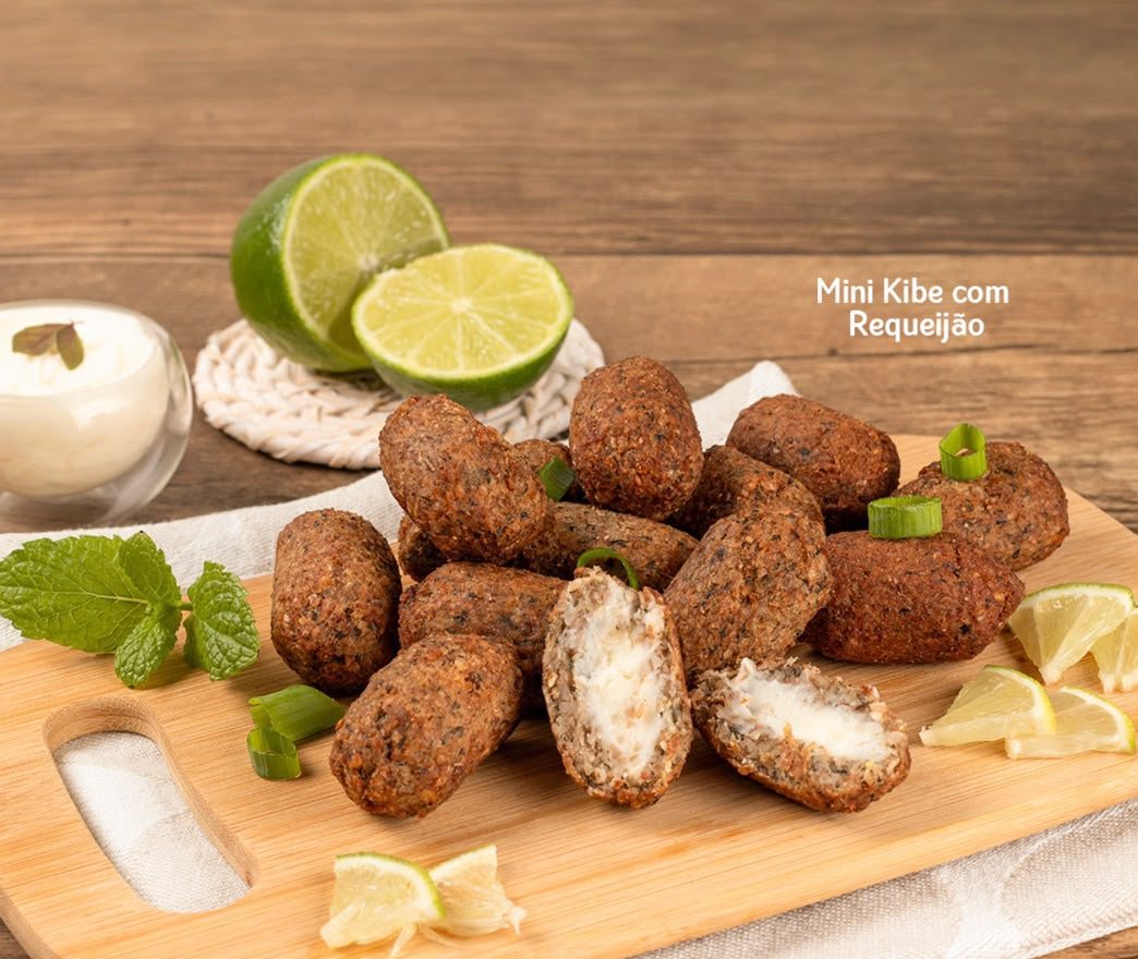 Mini kibes fritos sobre tábua de madeira, dois abertos mostrando o recheio de requeijão.